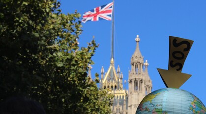 A paper globe with an arrow above it saying SOS being held up at a protest on a bright sunny day outside Parliament with the Union Flag flying high