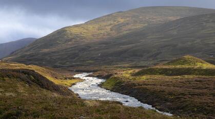 A fast moving stream flows through the atmospheric wild landscape of the Scottish Highlands.