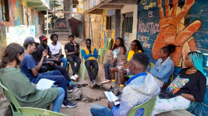 A youth group meeting outside with a community art work with a peace message on the wall beside them