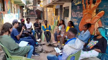 A youth group meeting outside with a community art work with a peace message on the wall beside them