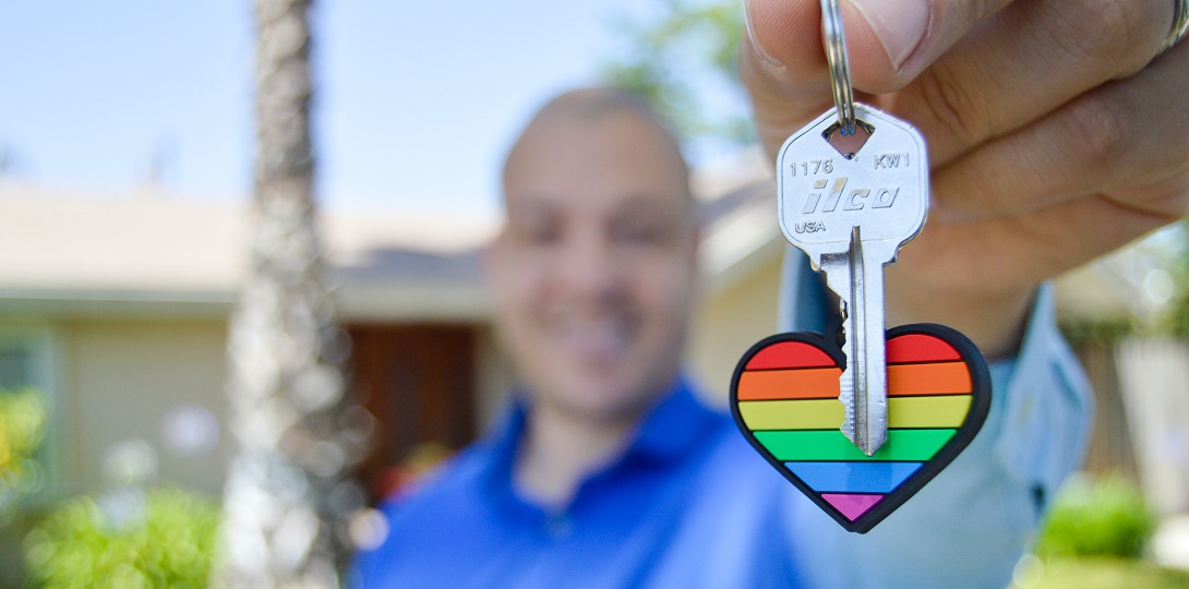 A man holding up a door key with a rainbow fob