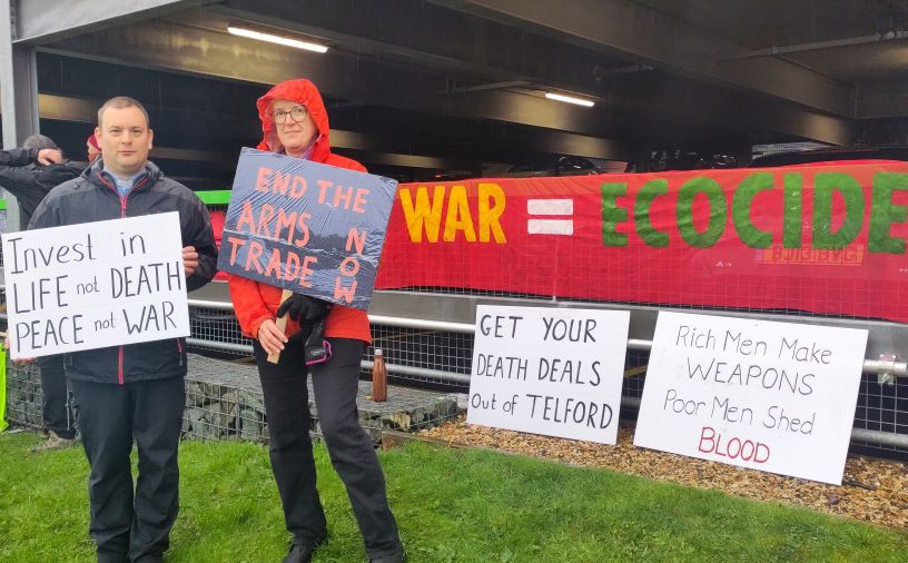 Two people in front of war=ecocide banner