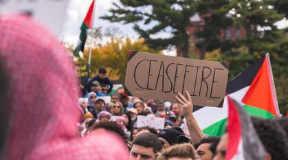 A cardboard sign saying 'CEASEFIRE' being held up at demonstration with Palestinian flags around