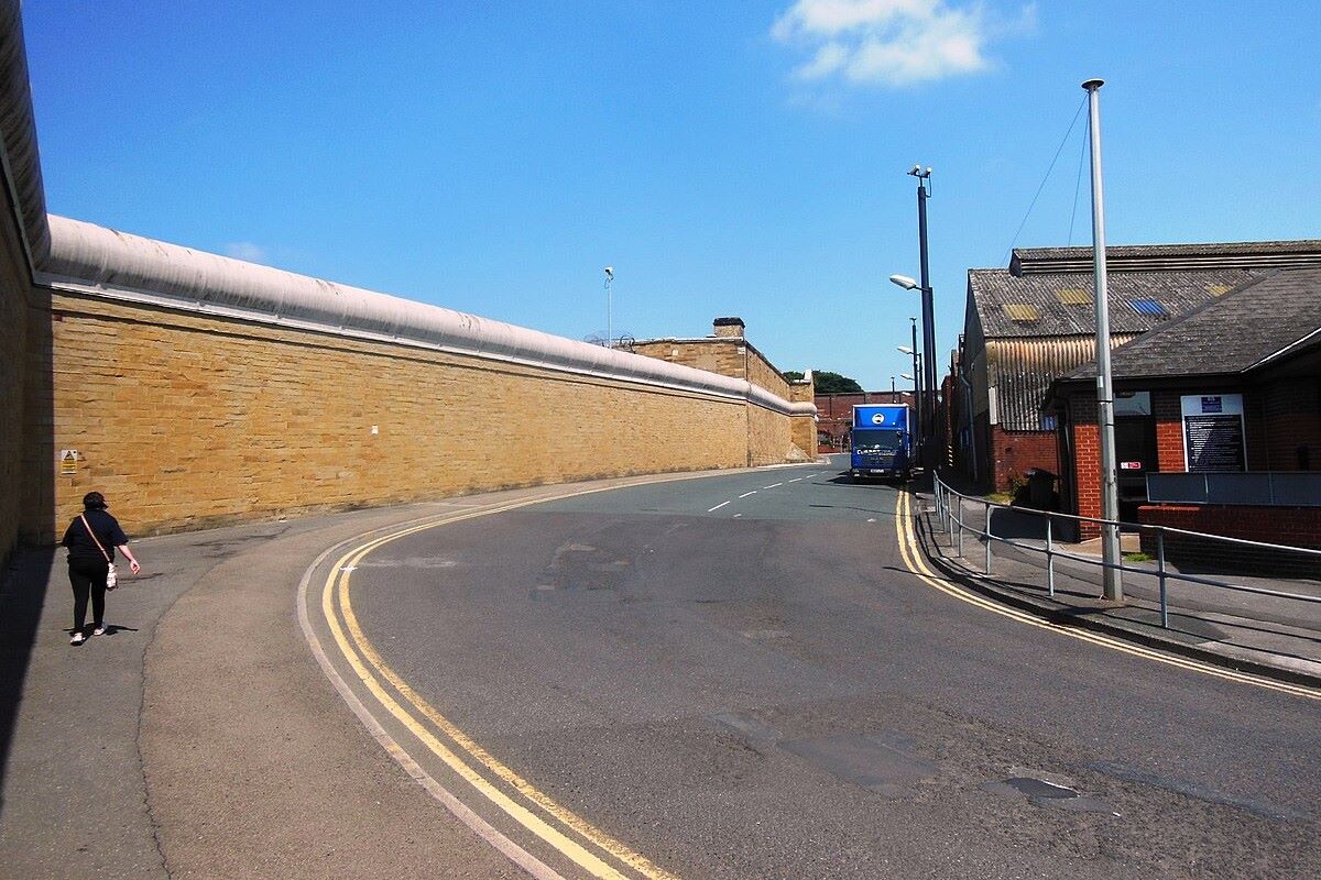 Prison wall with metal fencing and blue skies. 