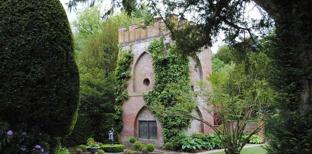 A stone tower in a garden covered with green climbing plants