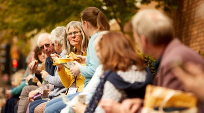 People of different ages sitting outside on a wall chatting while having lunch during Yearly Meeting