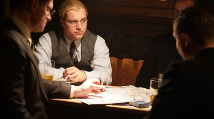 Bonhoeffer sat at a table in discussion. The table is covered in papers