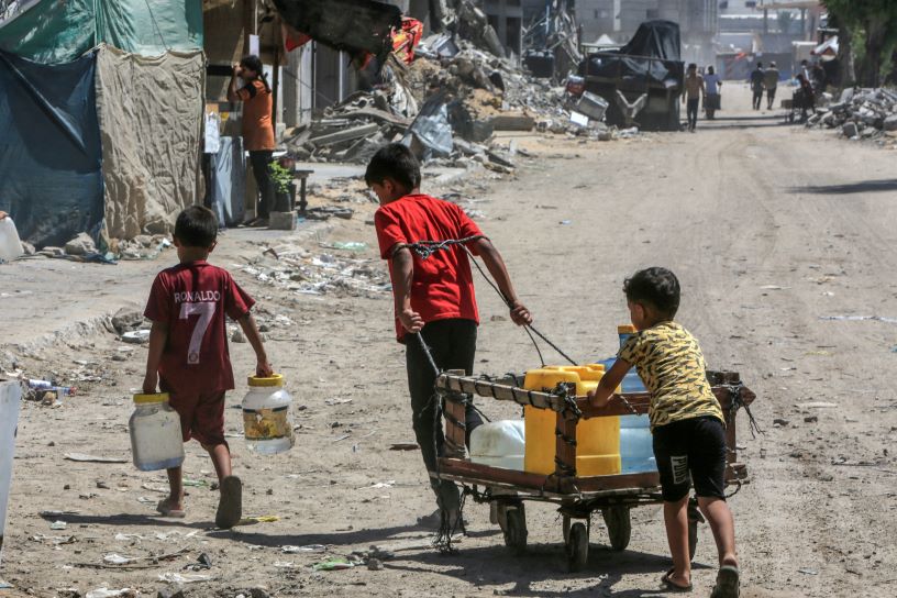 Young boys pushing water surrounded by destroyed buildings