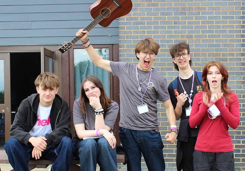 A group of young people outside the Frontier Centre. One holds a guitar aloft and pretend to scream. Image: Amy Beedle for Quakers in Britain