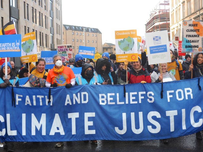People and large blue banner which reads Faith and Beliefs for Climate Justice