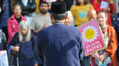 Shanon Shah of Faith for the Climate speaks, with his back to the camera, to an assembled group of campaigners who are listening carefully