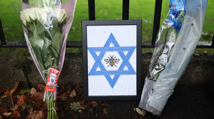 Flowers on a metal fence outside Heaton Park Synagogue, with a placard showing a bee within a blue star of David