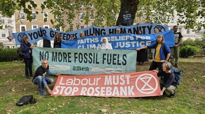 A group of interfaith campaigners in a park hold a set of banners reading Your Greed is Killing Humanity, Faiths and Beliefs for Climate Justice, No More Fossil Fuels Amen and Labour Must stop Rosebank