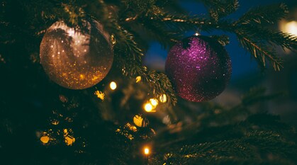 A close-up photo of two baubles, one beige and one purple, on a Christmas tree with fairy lights.
