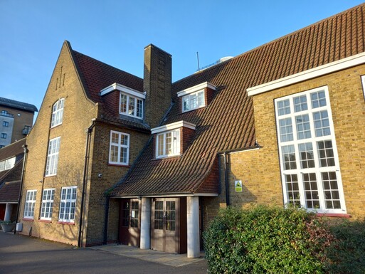 Brick building with long dual level windows and 'Friends Meeting House' lettering, building is situated on a busy road next to a cycle path. 
