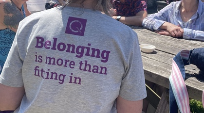 Close up of a person sat a picnic table wearing a Quaker T-shirt which says "Belonging is more than fitting in"