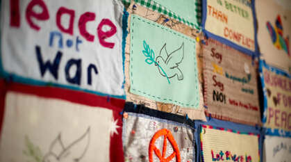 A closeup of a handmade fabric banner featuring a peace dove, the words 'peace not war' and other themed designs stitched on