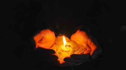 hands cupped around a candle which has spilled wax onto a piece of cardboard
