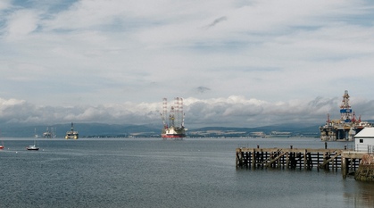 A view across Cromarty Firth with several oil rigs parked and sailing boats on mooring buoys
