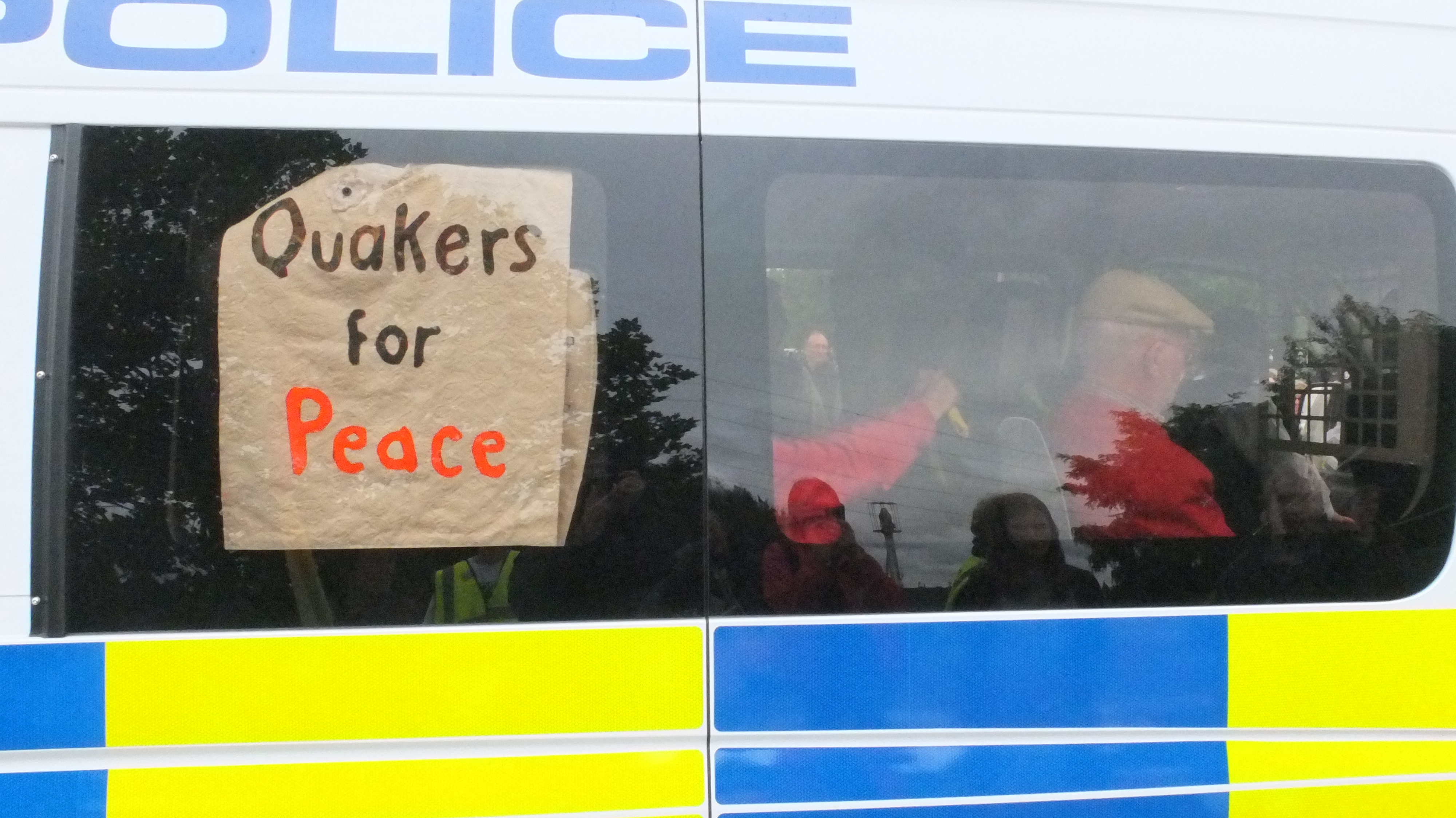 A picture of a Quaker inside a police van holding a sign which says Quakers for Peace.